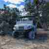 Grey 2024 Kawasaki Mule parked in some cedar trees.