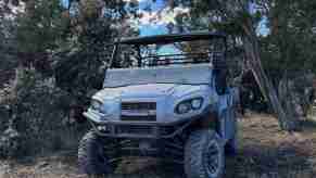 Grey 2024 Kawasaki Mule parked in some cedar trees.