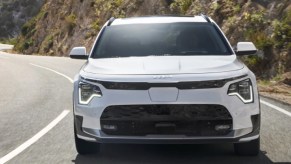 A white Kia Niro EV subcompact electric SUV is driving on the road.