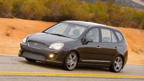 A black Kia Rondo driving down the road.