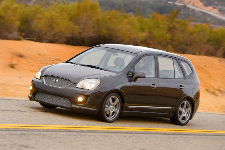 A black Kia Rondo driving down the road.