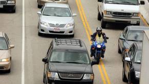 A motorcycle rider in safety gear engages in lane splitting on a California highway.