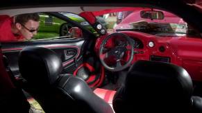 A spectator looking into the interior of a 1996 Mazda MX-3 coupe at the Darknights Nationals in Toronto