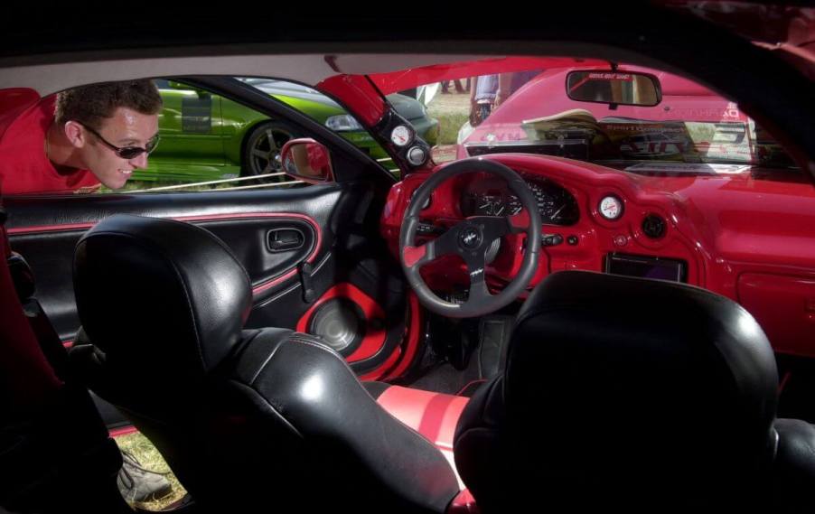 A spectator looking into the interior of a 1996 Mazda MX-3 coupe at the Darknights Nationals in Toronto