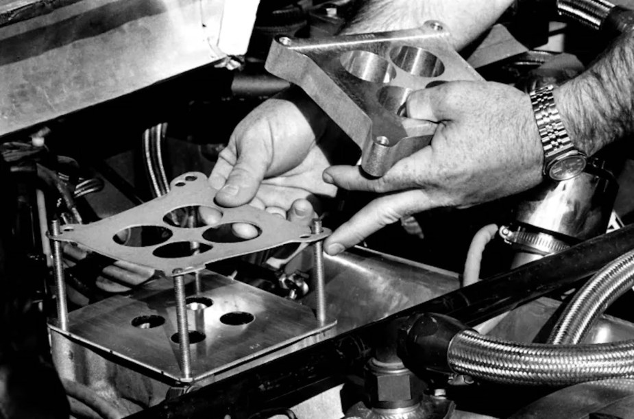 The hands of a NASCAR mechanic install the regulation restrictor plate on a V8 engine.