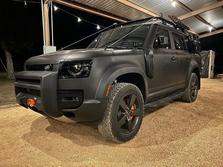 A matte black Land Rover Defender 130 sits under a pavilion at the TReK 2023 event in Texas.