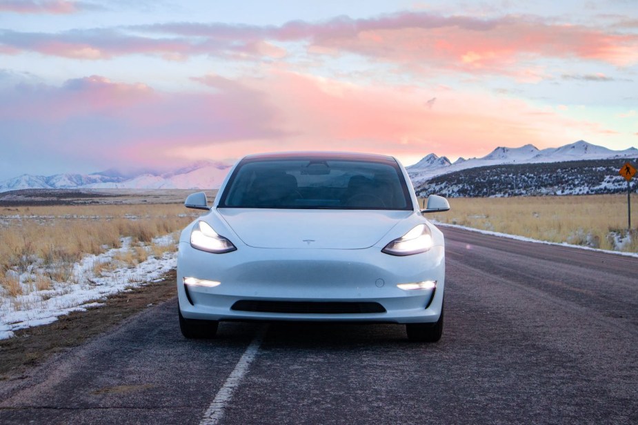 White Tesla EV parked on a snowy road, mountains visible in the backround.