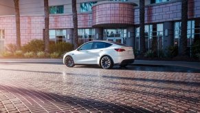 A white Tesla Model Y small electric SUV is parked on the street.