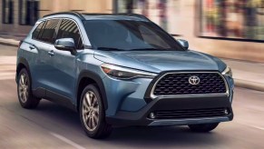 A blue Toyota Corolla Cross subcompact SUV is driving on the road.