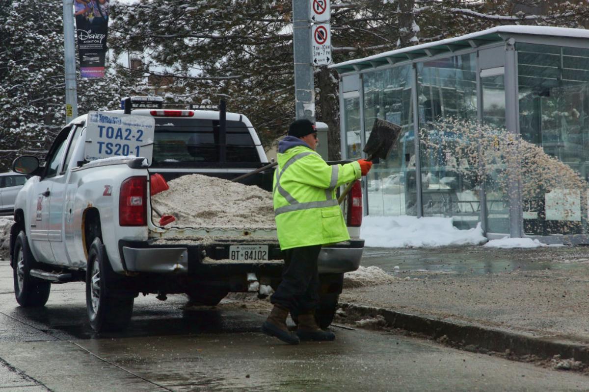 A worker pours road salt onto a street during winter.