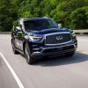 A 2024 Infiniti QX80 full-size luxury SUV model speeding down a highway framed by lush green trees