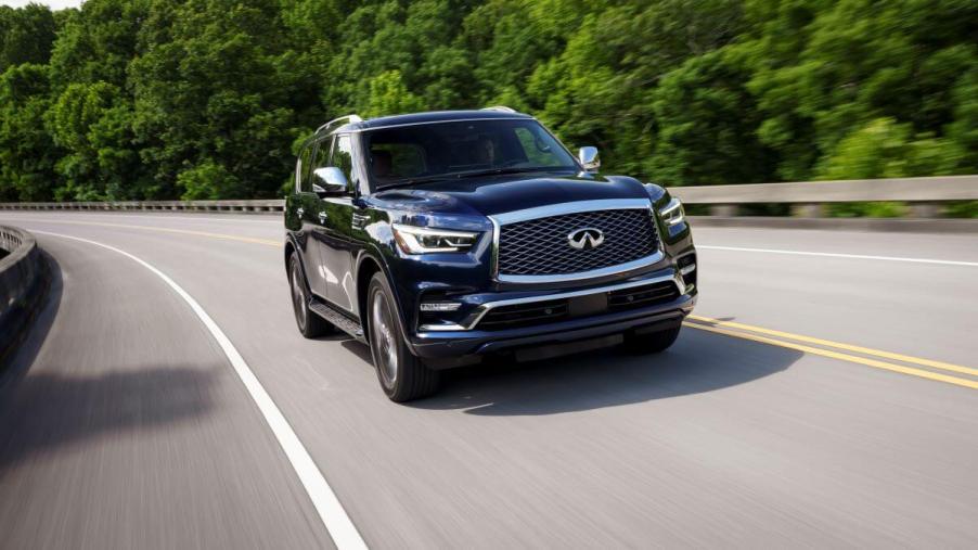 A 2024 Infiniti QX80 full-size luxury SUV model speeding down a highway framed by lush green trees