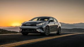 A 2024 Kia Forte GT compact sedan model parked on an asphalt country highway as the sun sets