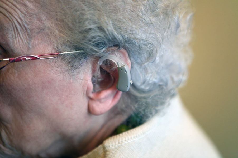 A woman with gray hair and glasses wearing an auditive hearing aid prosthesis on her left ear