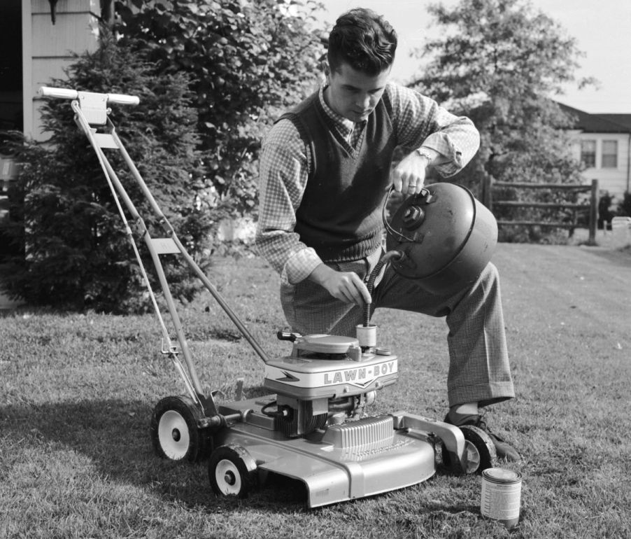 A black and white photo of a man mixing oil and gasoline to use his Lawn-Boy push mower model