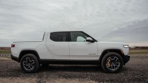 A side profile exterior shot of a Rivian R1T all-electric truck outside a manufacturing plant in Normal, Illinois