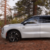 A side profile shot of a 2024 Mitsubishi Outlander PHEV compact SUV model parked on brush in a forest