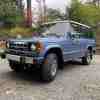 Blue vintage Mitsubishi Montero 4WD JDM first-gen SUV parked on gravel.