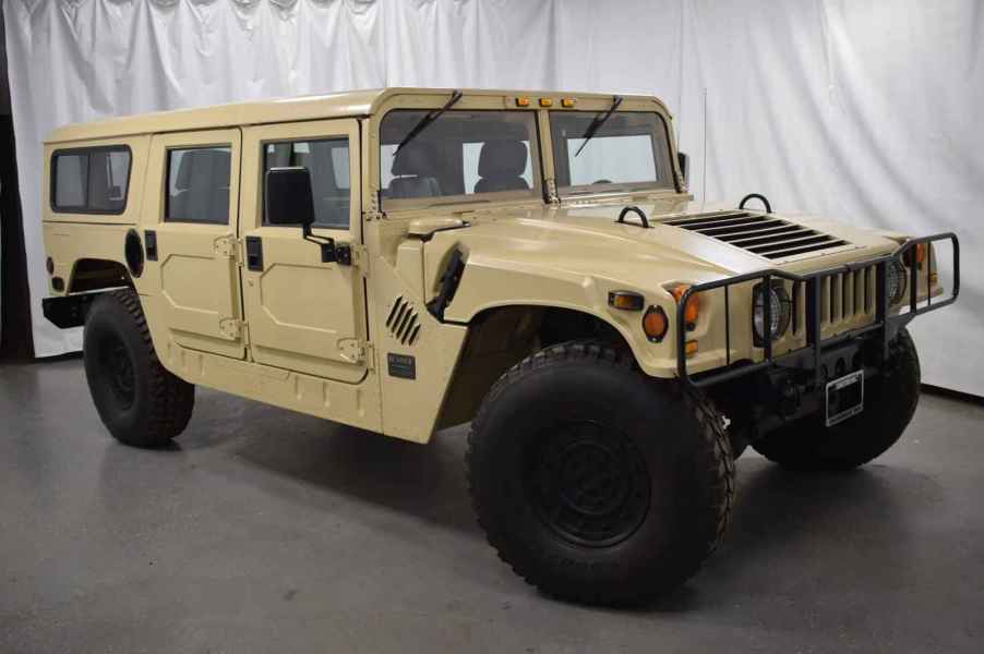 A desert tan 1992 Hummer H1 Humvee parked at right front angle in front of a white curtain