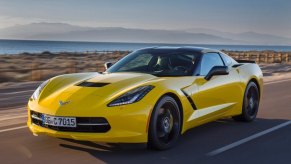 A yellow 2015 Chevrolet Corvette C7 Stingray cruises by a lake.