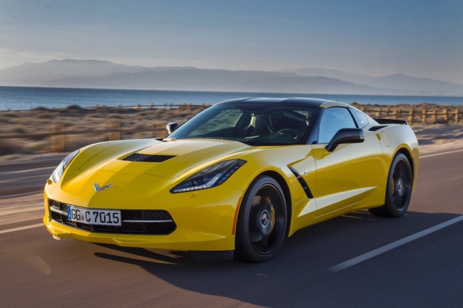 A yellow 2015 Chevrolet Corvette C7 Stingray cruises by a lake.