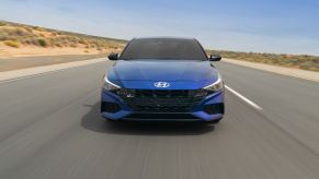 A blue 2023 Hyundai Elantra N driving down an empty road.