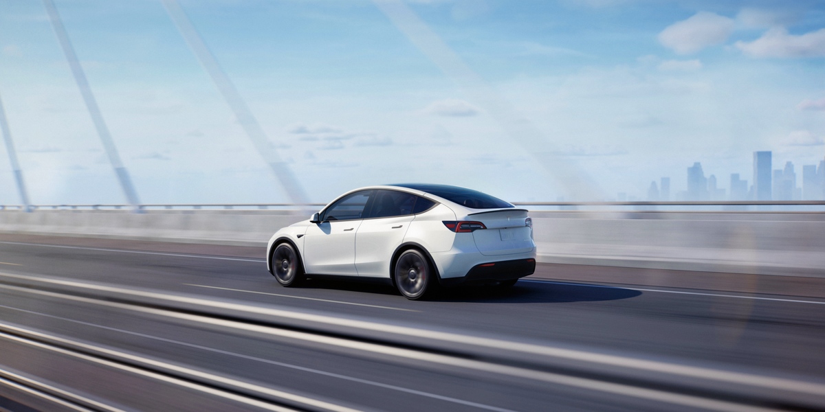 A white 2023 Tesla Model Y small electric SUV is driving on the road.