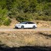 A white Volkswagen ID.7 driving on a desert road with some shrubbery in the background.