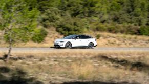 A white Volkswagen ID.7 driving on a desert road with some shrubbery in the background.