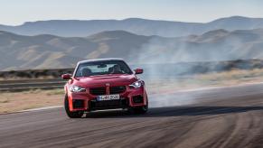 A red 2024 BMW M2 driving down a racetrack during the middle of the day.