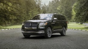 A black full-size SUV, the 2024 Lincoln Navigator, is parked outside surrounded by trees.