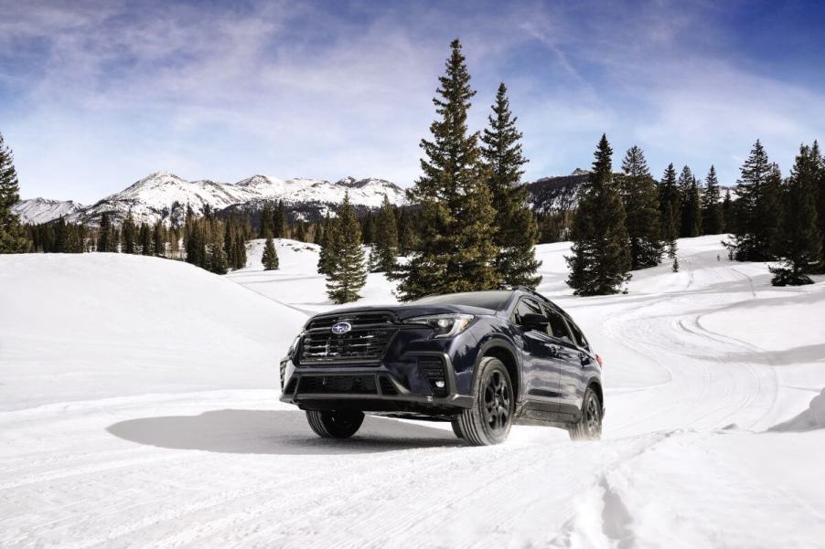 A 2024 Subaru Ascent midsize SUV model traversing in the snow among pine trees and mountains