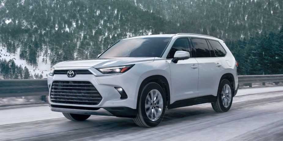 A white 2024 Toyota Grand Highlander midsize three-row SUV is driving on a snowy road. 