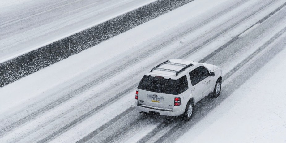 A white SUV is driving in snow. 