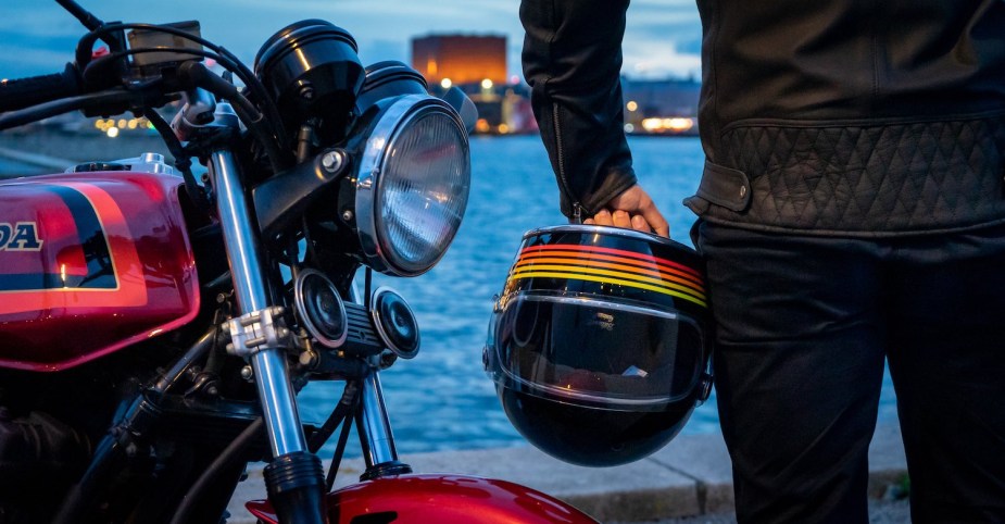 Motorcyclist holding a striped helmet next to a Honda bike.