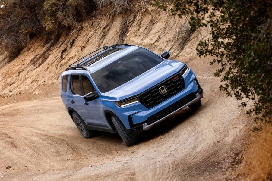 A blue Honda Pilot driving on a dirt road.