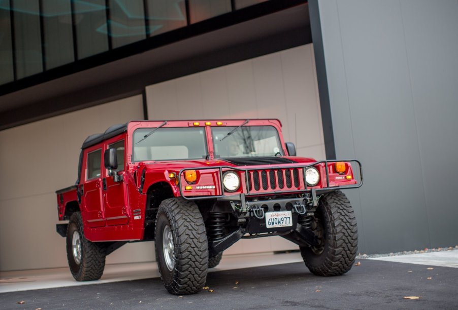 Red electric Hummer H1 SUV parked in front of a garage.