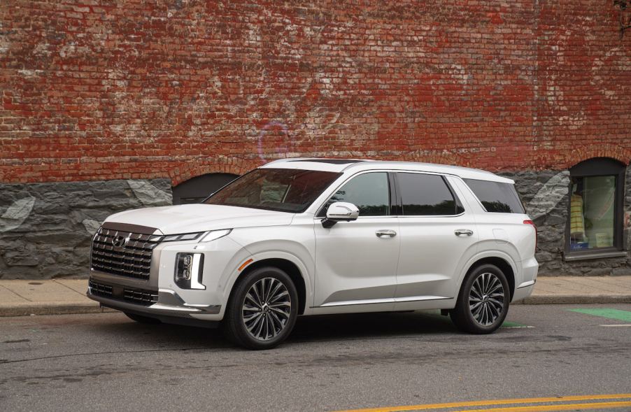 A white 2023 Hyundai Palisade parked next to a brick wall. This is one of many Hyundai SUVs.