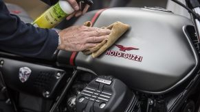 A rider polishes a Moto Guzzi V7 cafe racer motorcycle.