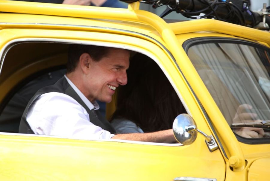 Tom Cruise, a famous movie star and celebrity, sits in a classic car on set of a movie.