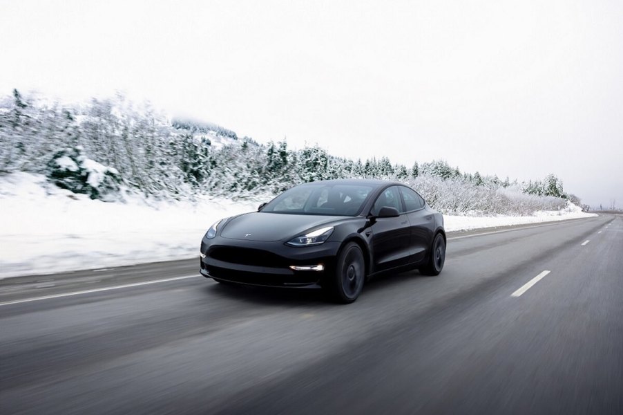 A black 2023 Tesla Model 3 electric car drives across a snowy landscape.