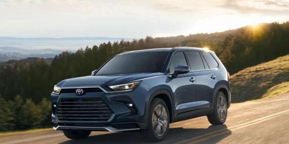 A blue 2024 Toyota Grand Highlander midsize three-row SUV is driving on the road. 