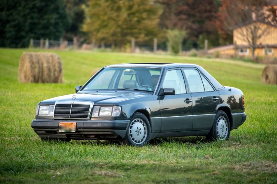 A dark gray classic W124 Mercedes parks on a lawn.