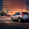 A 2024 Cadillac XT4 subcompact luxury SUV model driving at night through a city near a green streetlight