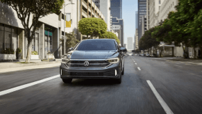 A 2024 Volkswagen Jetta compact sedan model driving through an urban city landscape