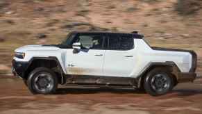 A white Hummer EV Pickup drive in left profile view off-road in desert-like terrain