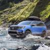 A 2024 Honda Passport TrailSport midsize off-road SUV model traversing a river in grassy mountains