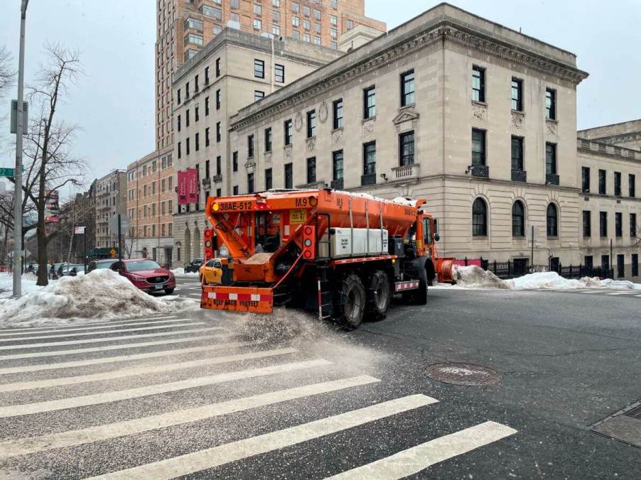 A sanitation department truck spreading road salt and and on city car roads