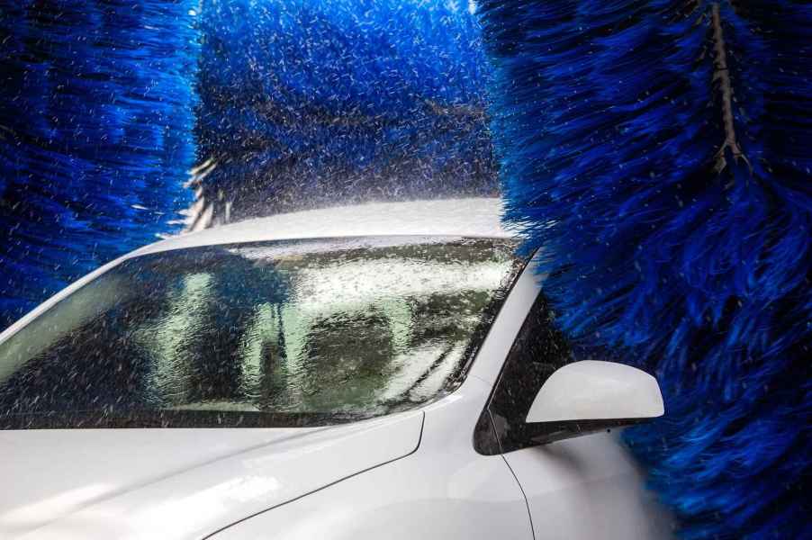 A white car shown in close left front angle in a touch car wash with blue brushes