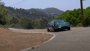 Green 1974 Ferrari Dino driving around a corner on a road.